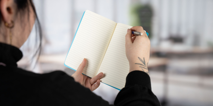Person hält ein personalisiertes Notizbuch in der Hand und schreibt mit einem Kugelschreiber darin