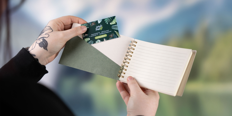 Person hält personalisiertes Notizbuch im A6-Format in der Hand und steckt eine Visitenkarte in die Innentasche des Covers