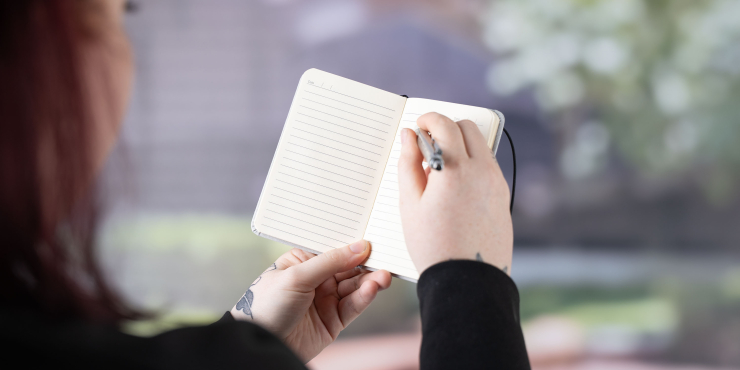 Person schreibt mit einem Kugelschreiber im offenen Carson Notizbuch im personalisiertem Design