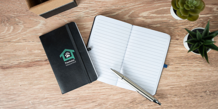 Notizbuch im A6-Format im individuellen Design offen und geschlossen auf einem Tisch worauf ein silberner Kugelschreiber liegt 