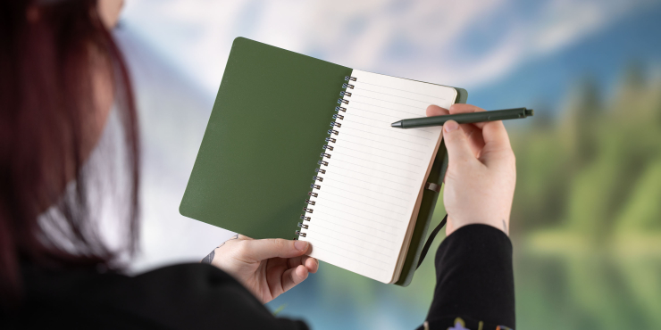 Person schreibt mit einem Kugelschreiber in das personalisierte Höga Repreve®-Notizbuch in A5-Format