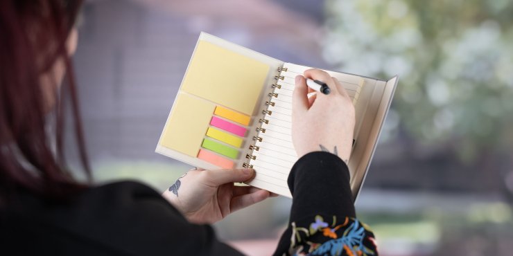 Person schreibt mit Kugelschreiber im B6-Notizbuch personalisiert und mit Haftnotizen auf der Innenseite