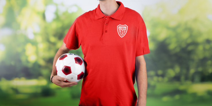 Mann hält einen Fußball in den Händen und trägt das Vereinslogo am Poloshirt