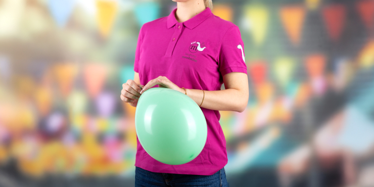 Frau ist dabei einen Luftballon zuzuknoten und trägt ein rosa Poloshirt