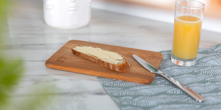 Frühstücksbrett aus Holz mit einem Butterbrot und Orangensaft