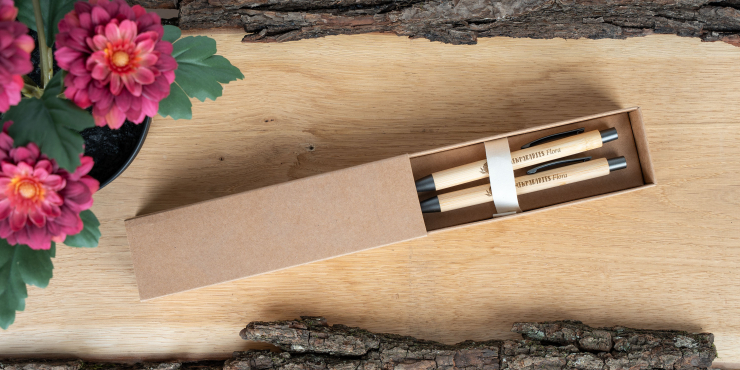 Bambowie Schreibset mit individueller Lasergravur in einer Schachtel auf einem Holzbrett neben pinken Blumen