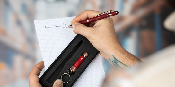 Person schreibt mit dem Kugelschreiber mit Logo auf einem Notizbuch