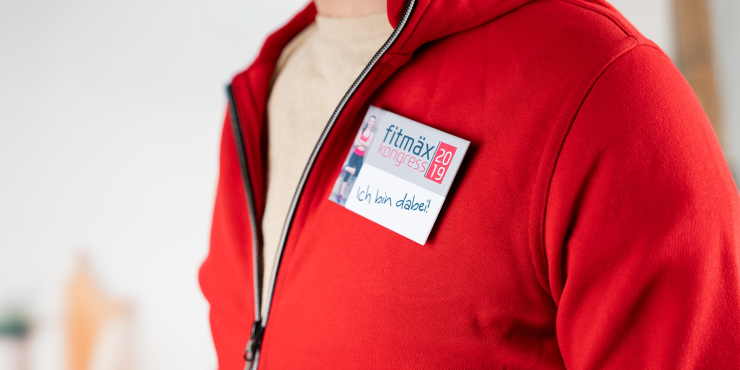 Personalisiertes Namenschild als Button mit Anstecknadel auf einer roten Weste 