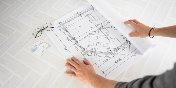 Laminierter CAD-Bauplan wird von einer Person auf Fliesen aufgerollt