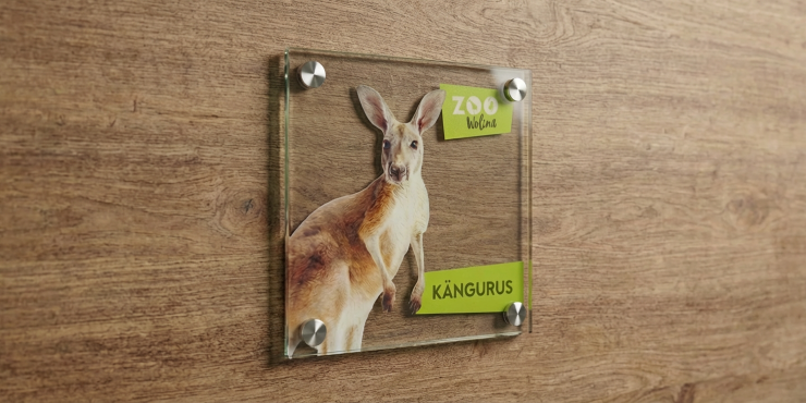 Holzwand an der ein personalisiertes Echtglasschild angebracht ist mit partiellem Weißdruck. Darauf zu sehen ist ein Känguru für die Bewerbung eines Zoos.
