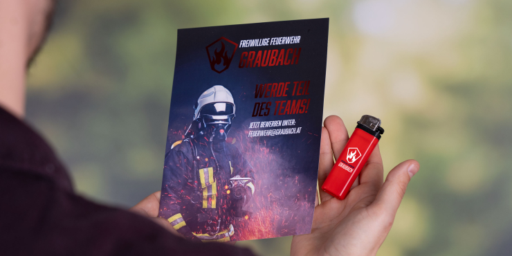 Person hält einen Flyer und ein bedrucktes Feuerzeug von der Feuerwehr