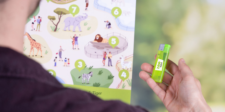 Mann hält bedrucktes Feuerzeug und einen Plan eines Zoos in der anderen Hand