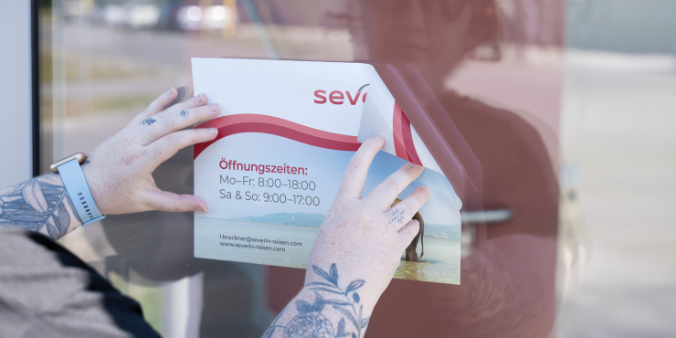 rechteckige, beidseitig bedruckte Blockout-Klebefolie wird von zwei Händen auf eine Glasscheibe geklebt