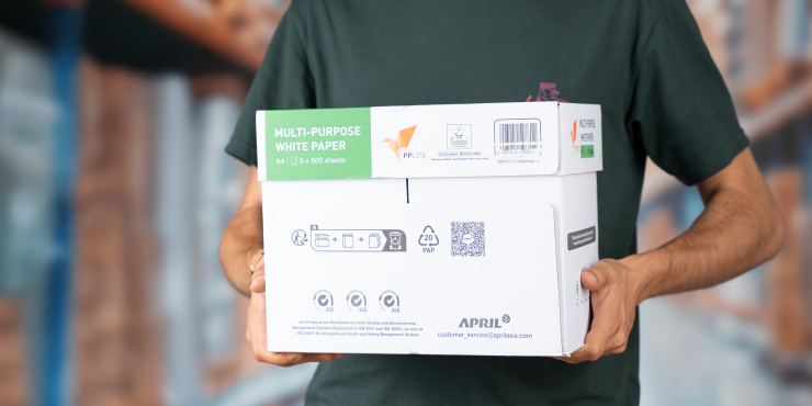 Mann hält eine Packung Kopierpapier Basic, im Hintergrund ist eine Lagerhalle