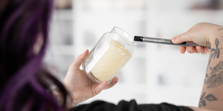 Person zündet eine Kerze in einem Glas mit einem BBQ Slim Metallic Feuerzeug an