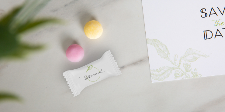 Individuell bedrucktes Flowpack mit zwei Frucht-Mentos auf weißer Marmorplatte daneben liegt eine Einladungskarte 