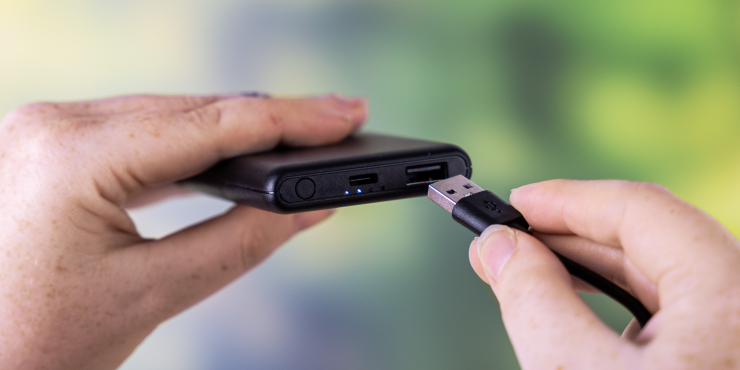 Hände stecken USB-Kabel an laufender Powerbank an 
