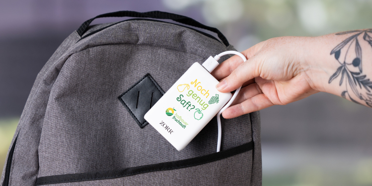 Person gibt gerade die personalisierte Powerbank in ihren grauen Rucksack