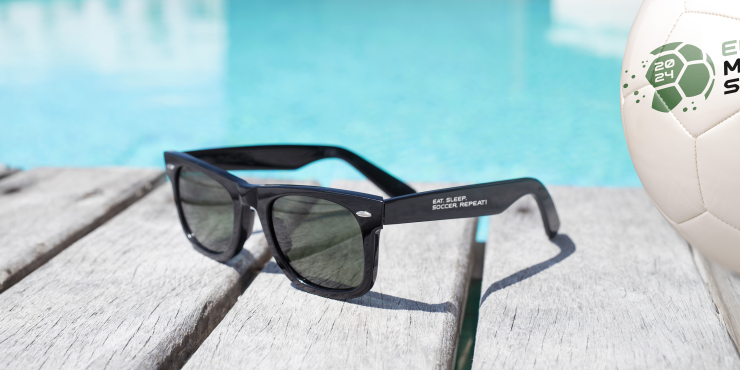 Schwarze Sonnenbrille mit aufgedrucktem Logo liegt auf einem Holztisch