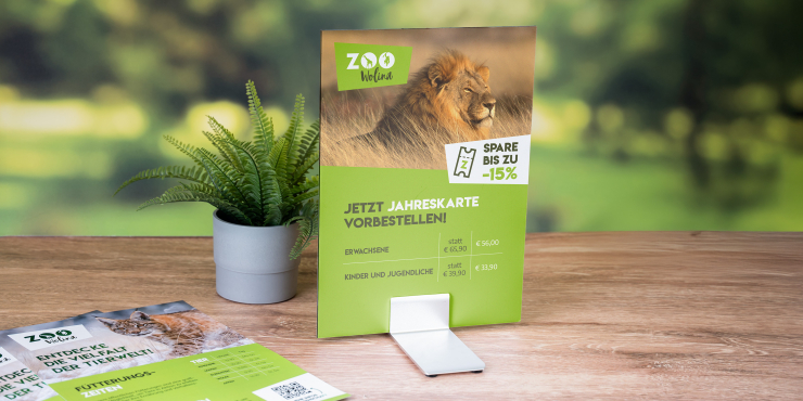 Personalisiertes Schild im Hochformat auf einem Aluminium-Standfuss neben weiteren Schildern auf einem Holztisch und einer Pflanze im Topf draussen im Garten