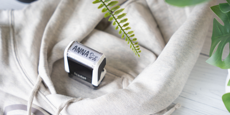 Personalisierter Textilstempel auf beigem Stoff neben grüner Pflanze