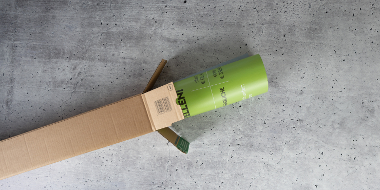 Versandhülse liegt auf grauem Hintergrund und das Produkt ist schon halb ausgepackt