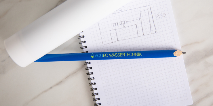 Ein bedruckter Zimmermannsbleistift liegt auf einem Notizbuch neben einer Papierrolle