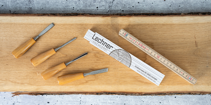 Weißer Zollstock mit Logo liebt neben Stemmeisen auf einem Holzbrett