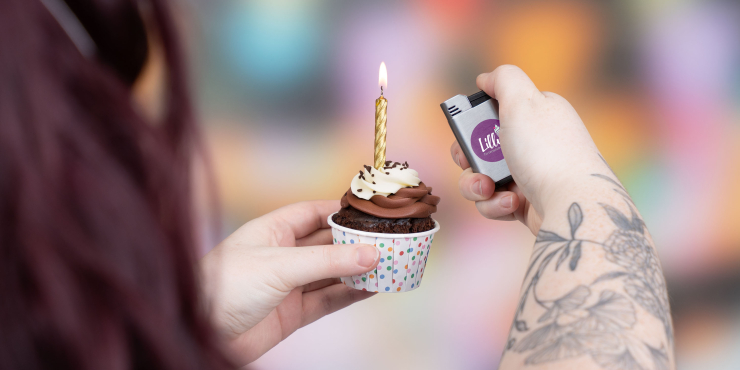 Person hält Quattro Jetflame Feuerzeug in der Hand und zündet eine Kerze auf einem Muffin an
