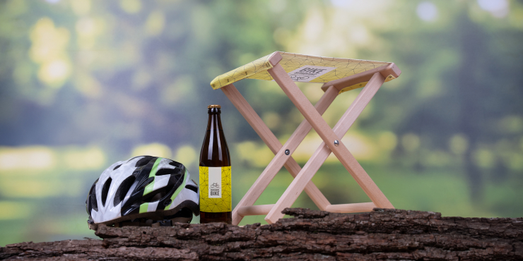 Holzhocker bedruckt mit Ihrem Design auf einem Baumstamm neben Bierflasche und Fahrradhelm