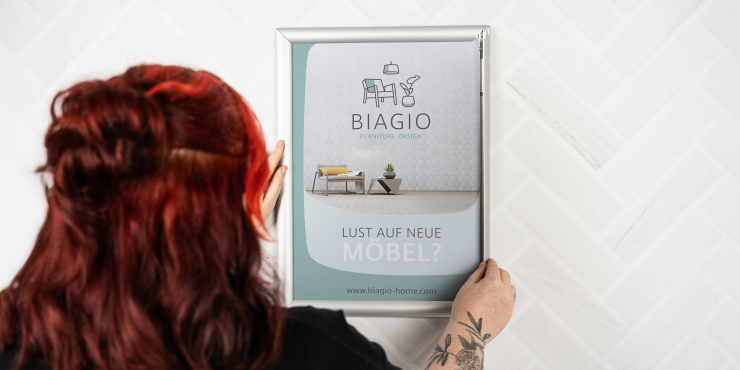 Frau befestigt bedrucktes Plakat im A3-Klapprahmen an der Wand