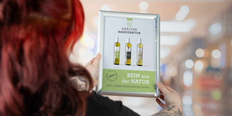 Frau befestigt bedruckte Plakat in A4-Klapprahmen auf einer Glasfront