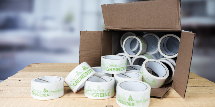 Großmengen an bedruckten Klebebändern liegen in einem geöffneten Karton