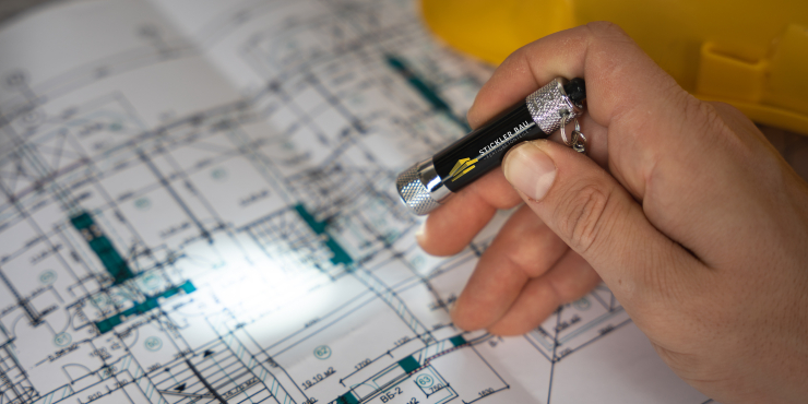Eine Person leuchtet mit einer bedruckten Schlüsselanhänger Taschenlampe auf einen Bauplan