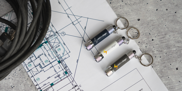 Mehrere Taschenlampen Schlüsselanhänger mit Druck liegen auf einem Bauplan