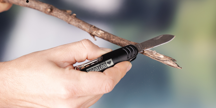 Eine Person schnitzt einen Stock mit einem bedruckten Cambridge Taschenmesser