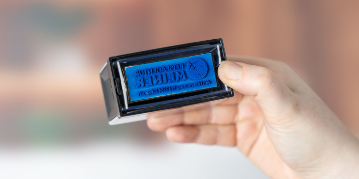 Person hält Colop Textstempel mit blauen Stempelmotiv in der Hand