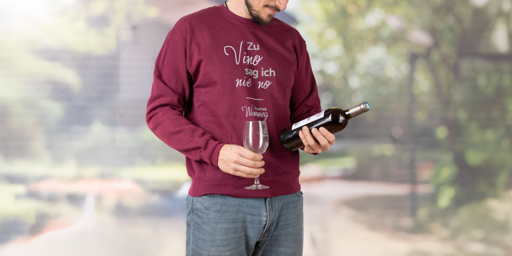 Weinliebhaber schaut sich eine Flasche Wein an und trägt weinroten Fruit of the Loom-Sweater, der auf der Vorderseite bedruckt ist