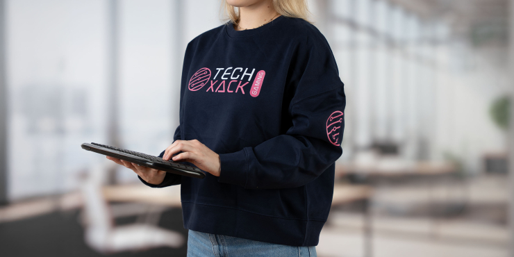 Weibliche Person steht im Büro und hat dunkelblauen Stanley/Stella-Hoodie mit vorderem Aufdruck an