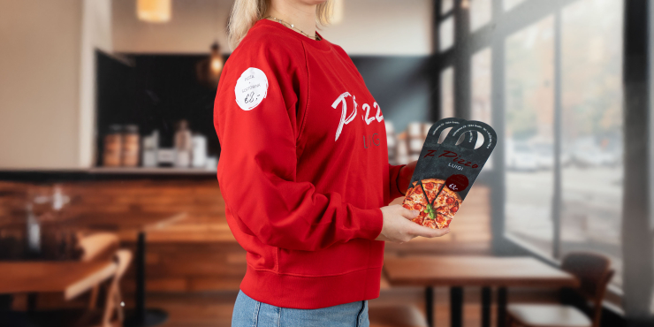 Weibliche Person steht in der Pizzeria und trägt einen roten Stanley/Stella-Sweater mit kreativem Aufdruck auf der Brust und am Ärmel
