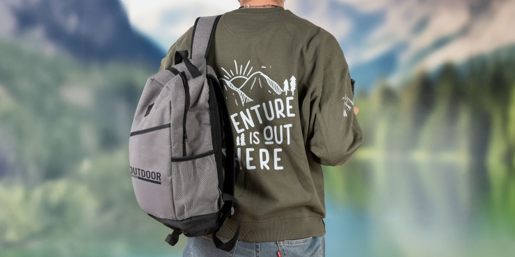 Männliche Person geht auf Wanderung, trägt einen Rucksack und einen olivfarbenen Stanley/Stella-Sweater mit Aufdruck am Rücken