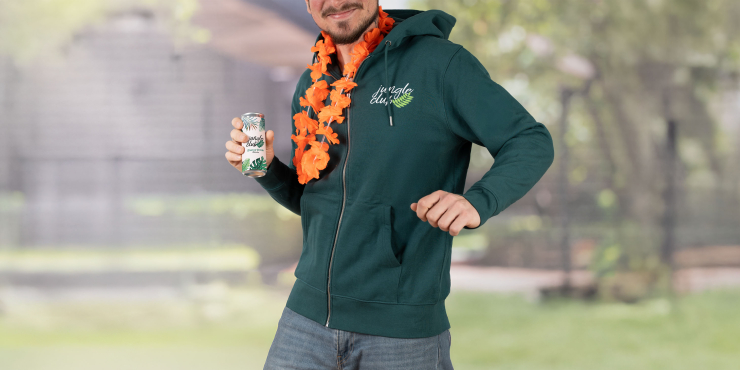 Männliche Person hält eine Dose und trägt einen dunkelgrünen Stanley/Stella-Zip-Hoodie, der auf der linken Brustseite bedruckt ist