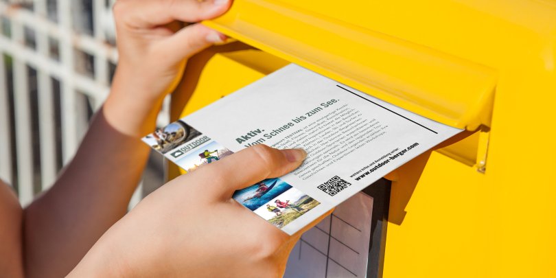 Jemand wirft bedruckte Postkarte in den Postkasten