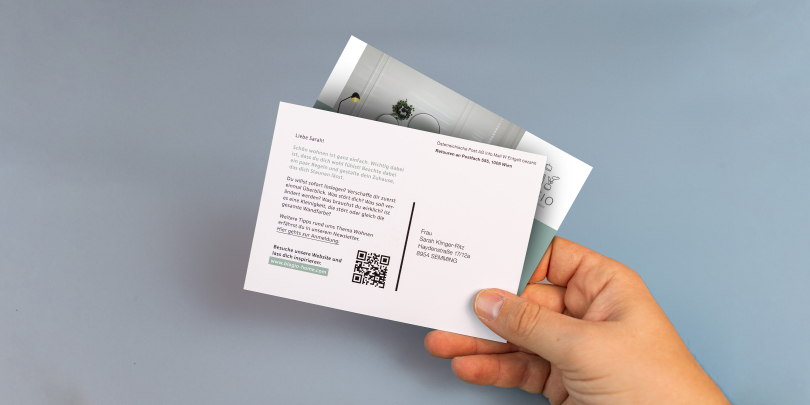 Jemand hält bedruckte Postkarten auf grauem Hintergrund