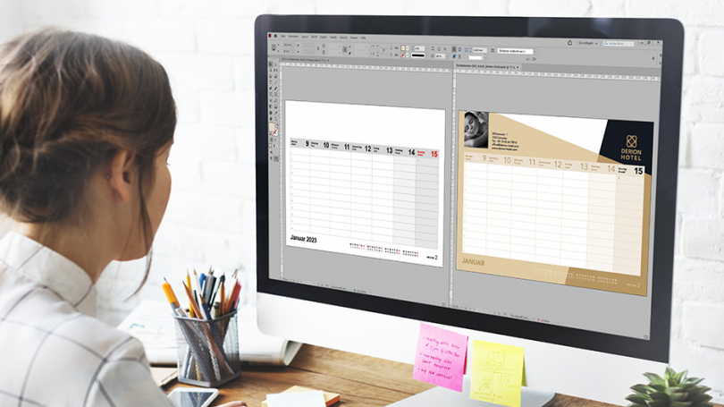 Eine Frau sitzt vor einem Bildschirm. Auf diesem sind zwei Kalenderseiten in Adobe InDesign geöffnet.