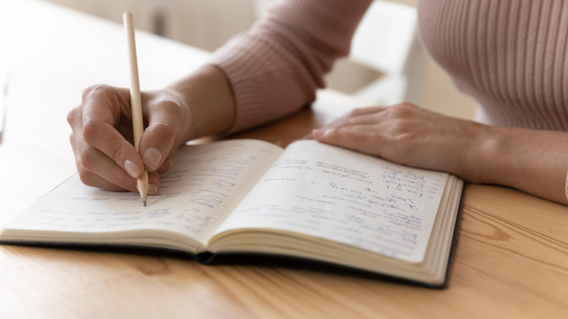 Eine Person schreibt mit einem Stift in ein Notizbuch.