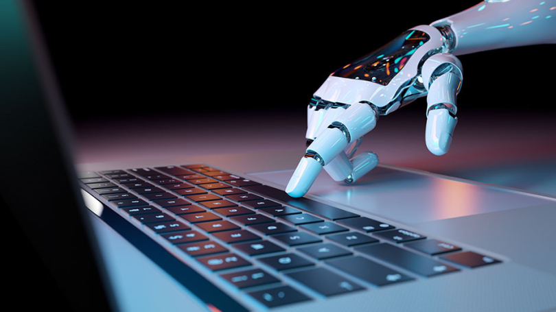 Eine Roboter-Hand berührt die Tasten eines Laptops.