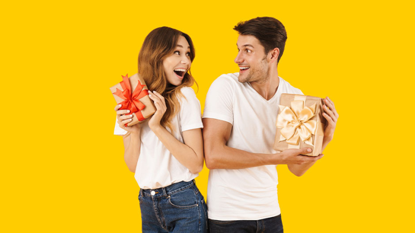 Eine Frau und ein Mann halten jeweils ein Geschenk in der Hand und schauen sich erfreut an.